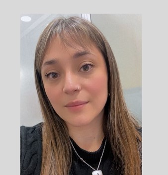 Close-up portrait of a woman with light brown hair and bangs, wearing a black sweater and a silver necklace, looking at the camera.